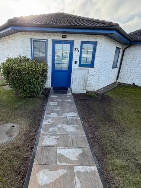 Das Ferienhaus Meeresbrise von vorn, mit blauer Haustür und eigenem Plattenweg