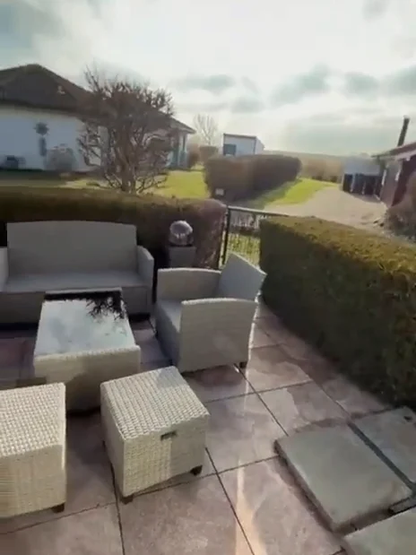 Sonnenterrasse mit Loungemöbeln, Hecke und Blick über die Ferienhaussiedlung