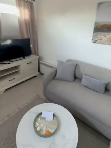 Wohnbereich mit hellem Sofa, Fernseher und Nordseebild unter offenem Balkendach